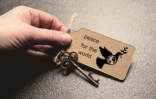 A hand holding a wooden tag with the text "peace for the world" and a dove graphic, alongside a decorative key.