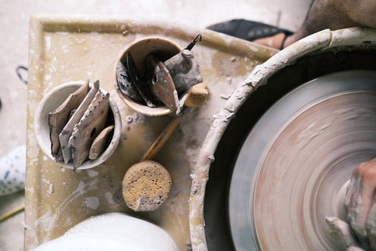 Aerial view of pottery tools on a potter's wheel, including wooden tools and sponges in ceramic containers.