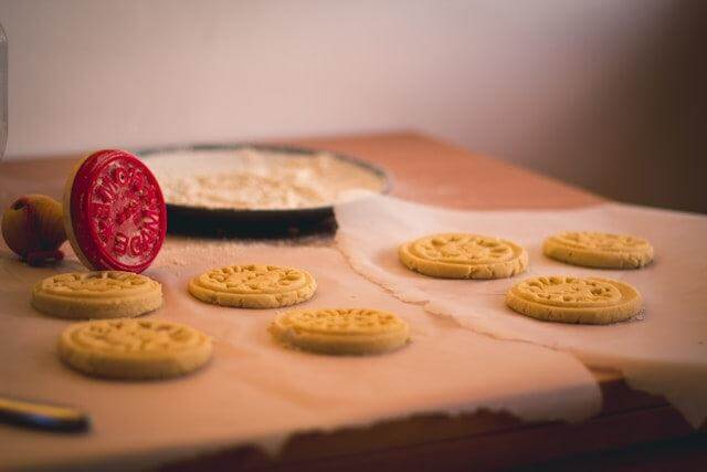 Custom baking stamps imprinting cookies on parchment paper in a cozy kitchen setting.