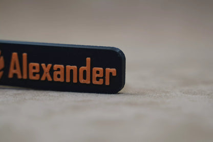 Close-up of a personalized keychain featuring the name "Alexander" in bold orange lettering on a black background.