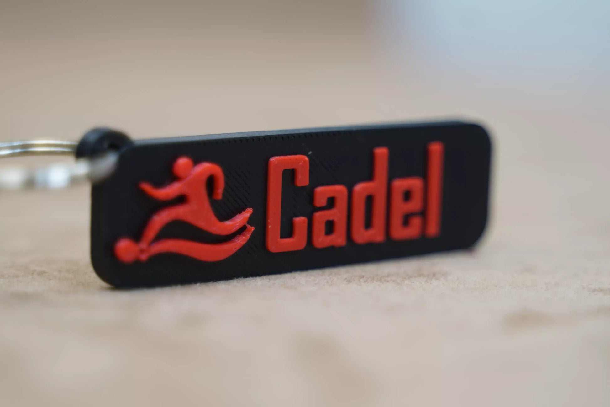 Personalised keychain with red 'Cadel' text and sports figure design on a black background.