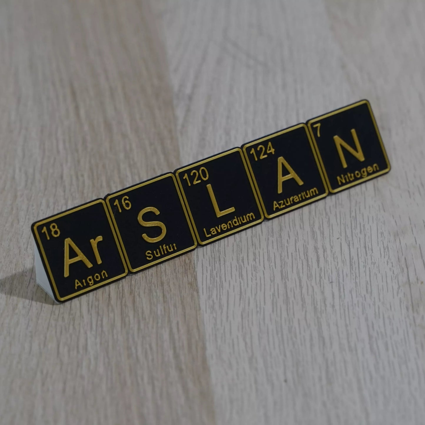 Personalised Periodic Table desk name plate spelling 'ARSLAN' with unique elements on a wooden surface.